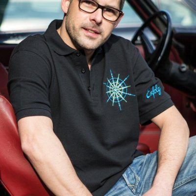 Poloshirt für Männer schwarz mit Kristall Erfolg gestickt in Blautönen sitzend im Auto